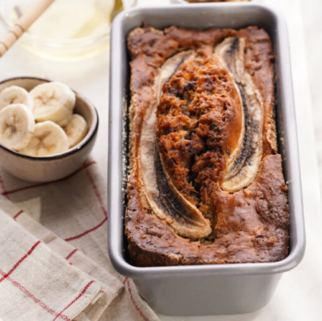Bananenbrot mit einer längs aufgelegten Banane in einer Kastenform, daneben Bananenscheiben
