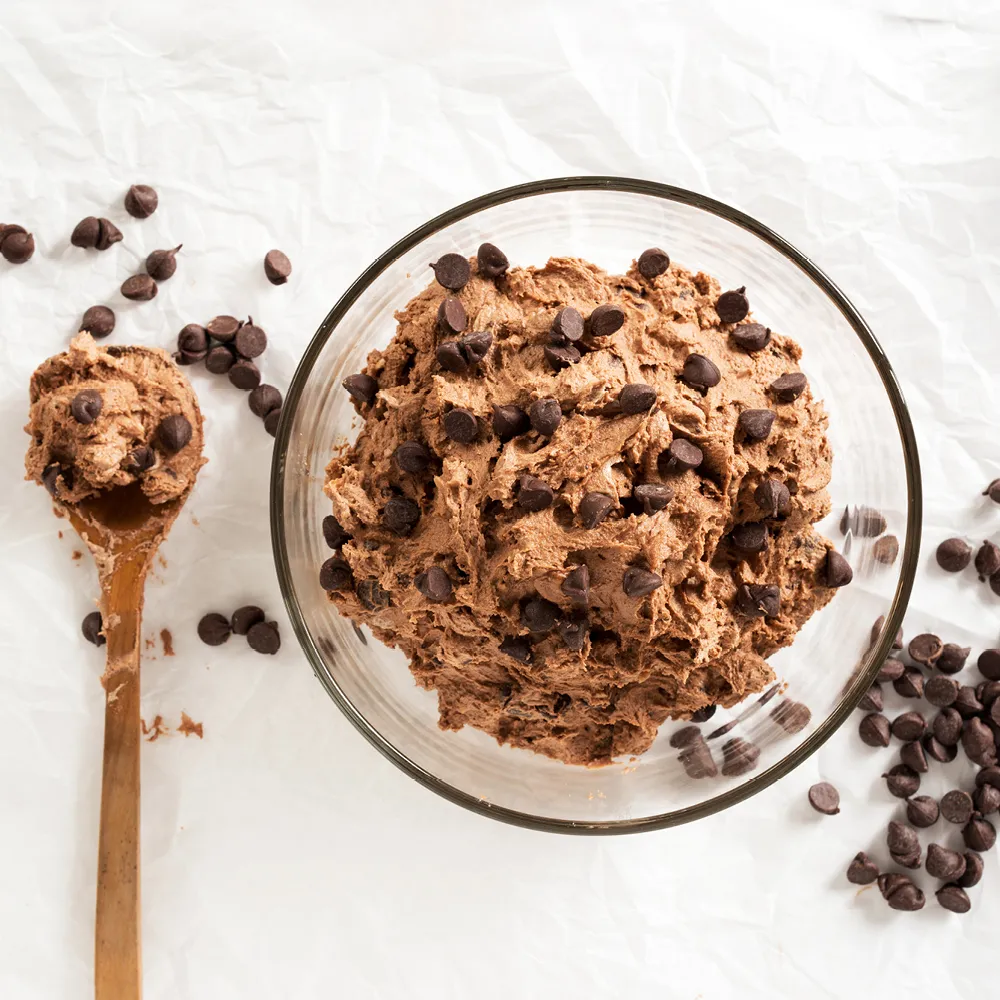 Schale mit Cookie Dough und Schokochips, daneben ein Holzlöffel