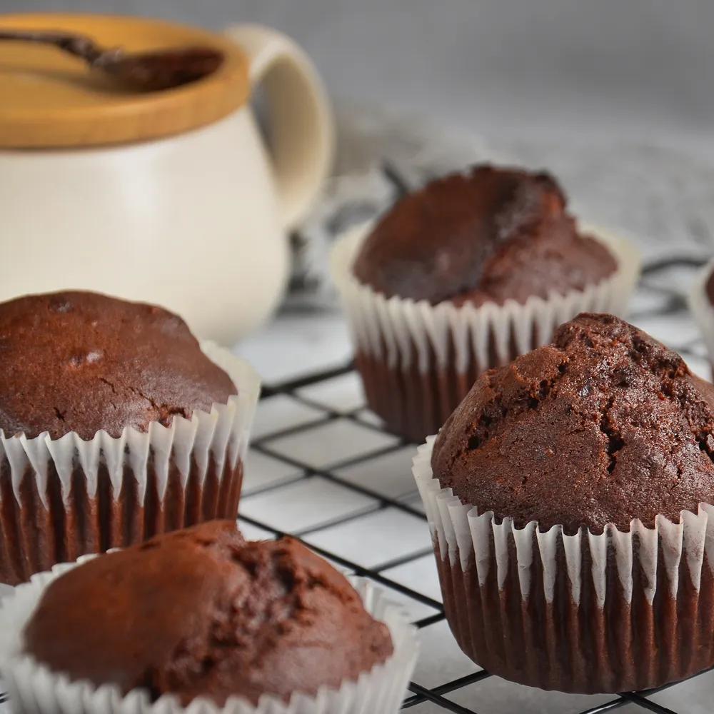 Drei Schokomuffins in weißen Papierförmchen auf einem Kuchengitter